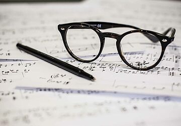 Brille und Stift liegen auf Notenblättern